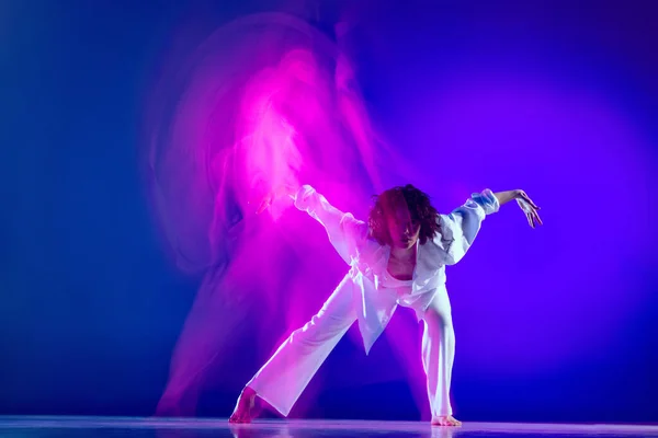 Dynamisch portret van mooi meisje, hiphop danser in witte outfit dansende hiphop geïsoleerd op blauwe achtergrond in roze neon licht. Jeugdcultuur, stijl en mode, actie. — Stockfoto