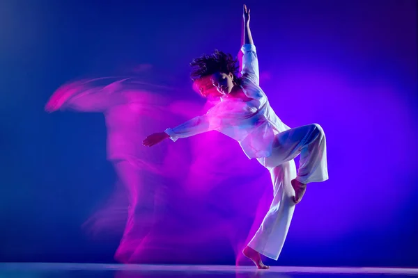 Dynamisch portret van mooi meisje, hiphop danser in witte outfit dansende hiphop geïsoleerd op blauwe achtergrond in roze neon licht. Jeugdcultuur, stijl en mode, actie. — Stockfoto