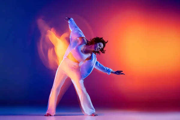 Deporte y belleza. Imagen de niña flexible, bailarina de hip-hop en traje blanco bailando hip hop aislado sobre fondo azul en luz de neón amarillo. — Foto de Stock