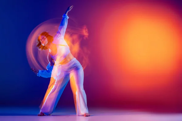 Street dancing. Image of flexible young girl, hip-hop dancer in white outfit dancing hip hop isolated on blue background in yellow neon light. Youth culture, style and fashion, action. — Stock Photo, Image