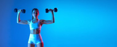 Spor ekipmanlarıyla genç sportif kız eğitimi neon ışıklarıyla izole edilmiş mavi-pembe stüdyo arka planında. Spor, eylem, fitness, gençlik konsepti.