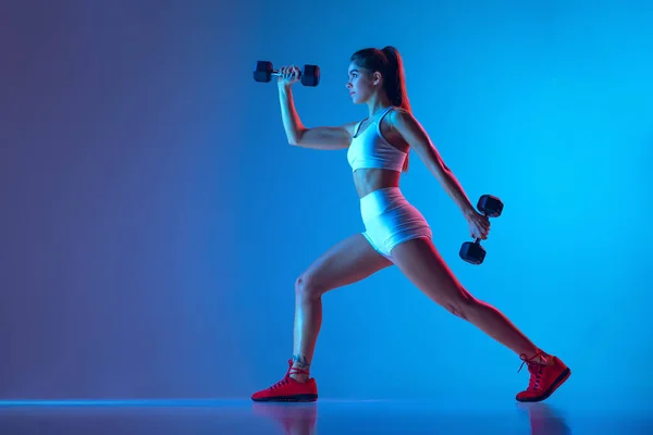 Молодая спортивная девочка тренировки со спортивным оборудованием изолированы на градиент сине-розовый студийный фон в неоновом свете. Спорт, экшн, фитнес, молодежная концепция. — стоковое фото