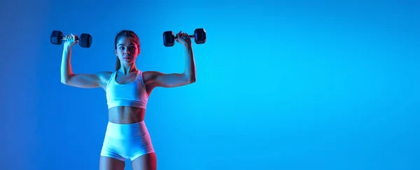 Treinamento de menina esportiva jovem com equipamentos esportivos isolados no fundo do estúdio gradiente azul-rosa em luz de néon. Esporte, ação, fitness, conceito de juventude. — Fotografia de Stock