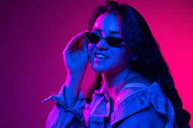 Güzel, genç, duygusal bir kız. Uzun koyu saçlı bir öğrenci. Neon ışıkta pembe-mavi bir arkaplanda izole edilmiş. Duygu kavramı, gençlik