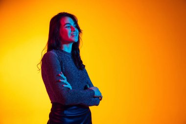 Güzel, heyecanlı genç bir kız, uzun siyah saçlı bir öğrenci, neon ışıkta sarı arka planda izole edilmiş. Duygu kavramı, gençlik