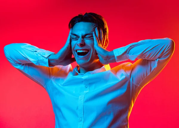 Retrato de meio-comprimento de jovem, estudante de camisa branca cabeça endurecida e gritando isolado sobre fundo estúdio vermelho em néon azul — Fotografia de Stock