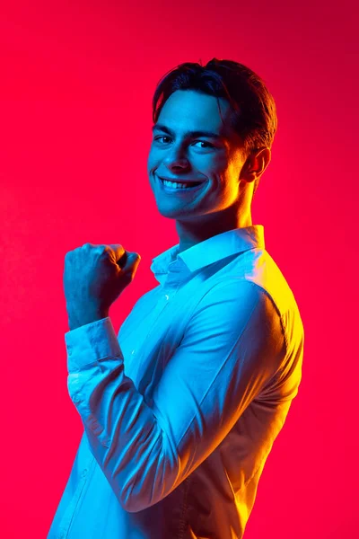 Muotokuva nuori komea mies valkoinen paita hymyillen, katsoen kameraa, poseeraa yli punainen sttudio tausta sininen neon valo — kuvapankkivalokuva
