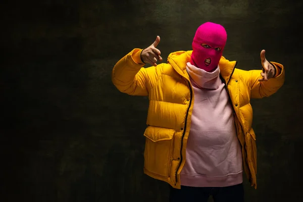 Prise de vue en studio d'un jeune homme anonyme portant une cagoule rose et une veste jaune, manteau isolé sur fond vintage foncé. Concept de sécurité, art, mode — Photo