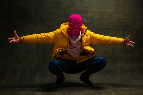 Prise de vue en studio d'un jeune homme anonyme portant une cagoule rose et une veste jaune, manteau isolé sur fond vintage foncé. Concept de sécurité, art, mode — Photo