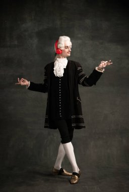 Çağdaş kulaklıklardaki ünlü besteci gibi peruk ve klasik ortaçağ kıyafetleri giyen genç bir adamın portresi koyu yeşil renkli arka planda izole edilmiş..