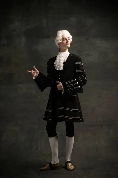 Młody człowiek w peruce i klasycznym średniowiecznym stroju jak słynny kompozytor odizolowany na ciemnozielonym tle vintage. Styl retro, porównanie koncepcji ery. — Zdjęcie stockowe