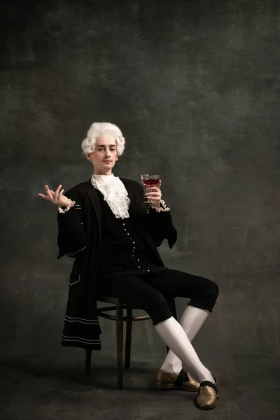 Schöner Mann im Bild der mittelalterlichen Person, Aristokrat Weinprobe isoliert auf dunkelgrünem Vintage-Hintergrund. Epochenvergleich. — Stockfoto