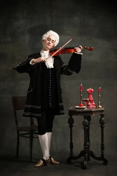 Jeune homme à l'image d'Amadeus Mozart, personnage médiéval isolé sur fond vintage vert foncé. Style rétro, comparaison des époques concept. — Photo