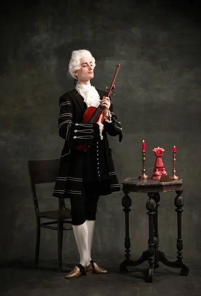 Retrato de jovem vestindo peruca e roupa medieval vintage como compositor famoso tocando violino isolado no fundo verde escuro do vintage. — Fotografia de Stock