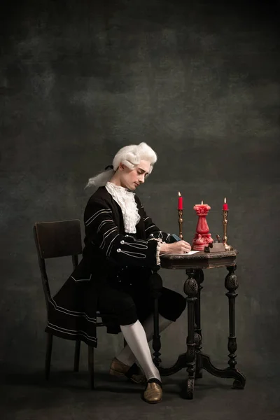 Młody człowiek na obraz Amadeusza Mozarta, średniowiecznego człowieka odizolowanego na ciemnozielonym tle vintage. Styl retro, porównanie koncepcji ery. — Zdjęcie stockowe