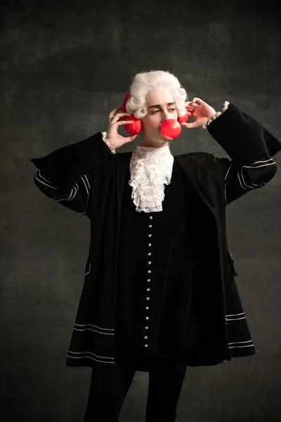 Portrait of young man wearing wig and vintage medieval outfit like famous composer having fun isolated on dark green vintage background. — Stock Photo, Image