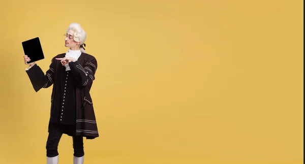 Portrait of young elegant man in white wig and vintage medieval outfit posing isolated on yellow background. Art, beauty, fashion — Stock Photo, Image