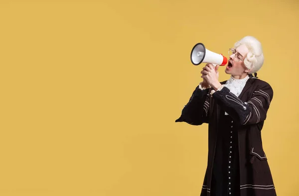 Retrato de jovem homem elegante em peruca branca e roupa medieval vintage gritando em megafone isolado em fundo amarelo. Arte, beleza, moda — Fotografia de Stock