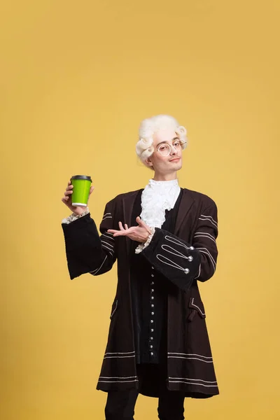 Retrato de hombre joven y elegante en peluca blanca y traje medieval vintage posando aislado sobre fondo amarillo. Arte, belleza, moda — Foto de Stock
