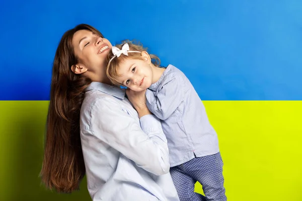 Портрет молодої жінки, мати з маленькою дівчинкою, дочка ізольована над синім і жовтим українським прапором. Ніякої війни — стокове фото