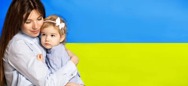 Портрет молодої жінки, мати з маленькою дівчинкою, дочка ізольована над синім і жовтим українським прапором. Флаєр — стокове фото