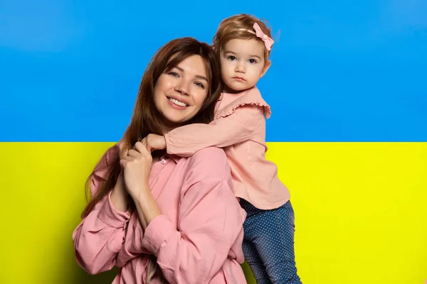 Portret młodej kobiety, matki z córeczką, córki odizolowanej na tle niebiesko-żółtej ukraińskiej flagi. Stop inwazji rosyjskiej — Zdjęcie stockowe