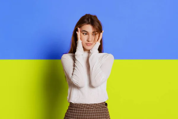 Portret van een jong meisje dat het hoofd aanraakt, tempels geïsoleerd over blauwe en gele Oekraïense vlag achtergrond. — Stockfoto