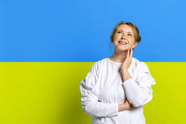 Retrato de joven hermosa chica con soñadora y reflexiva opresión facial aislada sobre fondo azul y amarillo. Feliz juventud ucraniana — Foto de Stock