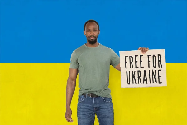 Концептуальний образ. Молодий чоловік тримає папір з написом "Свобода для України" ізольованим на тлі синього та жовтого прапорів. — стокове фото