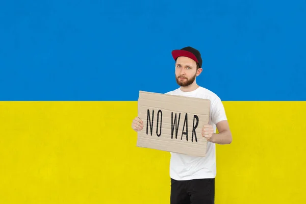 Konzeptionelles Bild. Junger Mann hält Tablette mit dem Schriftzug No War isoliert auf ukrainisch blau-gelber Flagge Hintergrund — Stockfoto