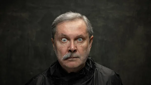 Retrato de un hombre mayor sorprendido mirando la cámara aislada sobre fondo oscuro vintage. Concepto de emociones, moda, belleza, auto reinvención — Foto de Stock