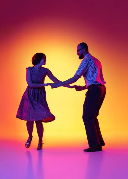 Retrato de hombre y mujer excitados, pareja de bailarines en trajes de estilo retro vintage bailando lindy hop danza aislada sobre fondo amarillo degradado y púrpura. —  Fotos de Stock