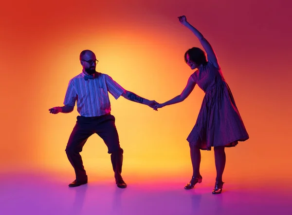 Portret van opgewonden man en vrouw, een paar dansers in vintage retro stijl outfits dansend lindy hop dans geïsoleerd op gradiënt gele en paarse achtergrond. — Stockfoto