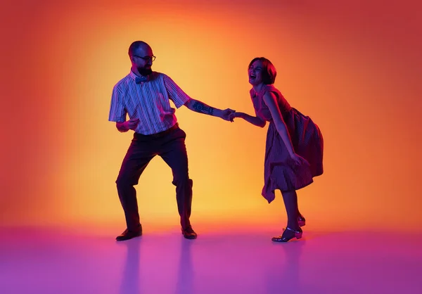 興奮した男と女の肖像、ヴィンテージレトロなスタイルの衣装を着たダンサーのカップルは、グラデーション黄色と紫の背景に隔離されたリンディホップダンスを踊る. — ストック写真