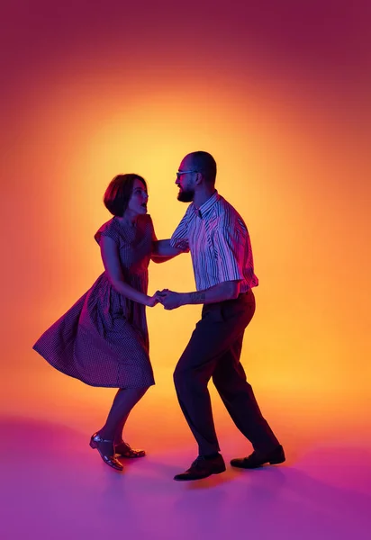 Portrait of excited man and woman, couple of dancers in vintage retro style clofits dancing lindy hop dance isolated on gradient yellow and purple background. — Stok Foto