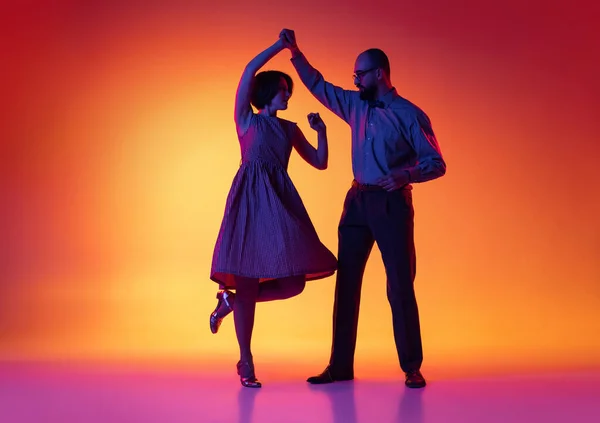 Retrato de hombre y mujer excitados, pareja de bailarines en trajes de estilo retro vintage bailando lindy hop danza aislada sobre fondo amarillo degradado y púrpura. — Foto de Stock
