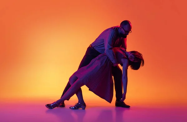 Портрет взволнованных мужчин и женщин, пара танцоров в винтажном стиле ретро, танцующих танец Линди-хоп, выделенный на градиентном желтом и фиолетовом фоне. — стоковое фото