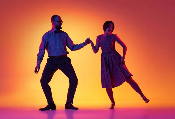 Retrato de homem e mulher animado, casal de dançarinos em roupas vintage estilo retro dançando dança lindy hop isolado no gradiente amarelo e roxo fundo. — Fotografia de Stock
