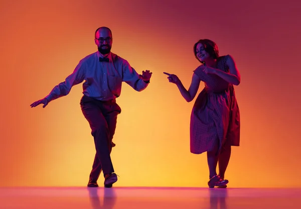 Portrait of excited man and woman, couple of dancers in vintage retro style outfits dancing lindy hop dance isolated on gradient yellow and purple background. — Stock Photo, Image