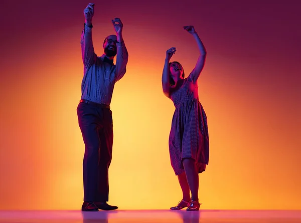 Portret podekscytowanego mężczyzny i kobiety, para tancerzy w klasycznym stylu retro stroje taniec lindy hop taniec odizolowany na gradientowym żółtym i fioletowym tle. — Zdjęcie stockowe