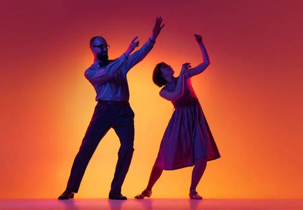 Portrait of excited man and woman, couple of dancers in vintage retro style outfits dancing lindy hop dance isolated on gradient yellow and purple background. — Stock Photo, Image