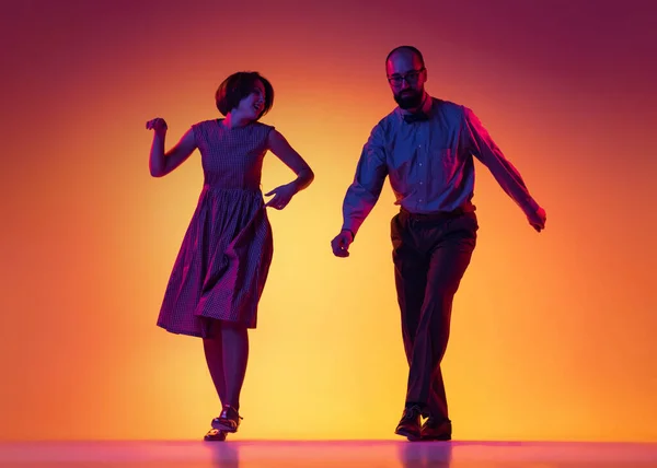 Portrait of excited man and woman, couple of dancers in vintage retro style outfits dancing lindy hop dance isolated on gradient yellow and purple background. — Stock Photo, Image