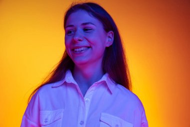 Gülümse. Beyaz tişörtlü güzel duygusal kızın portresi turuncu arka planda, neon ışıkta, filtrede izole edilmiş. Duygular, moda, gençlik kavramı