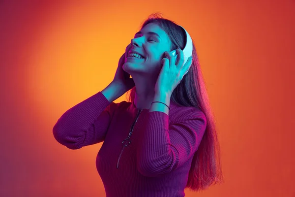 Portrét mladé krásné šťastné dívky ve sluchátkách poslech hudby izolované na oranžovém pozadí v neonovém světle, filtr. Pojetí emocí, hudby — Stock fotografie