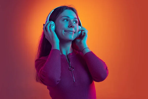 Портрет молодой красивой девушки в наушниках, слушающей музыку, изолированную на оранжевом фоне в неоновом свете, фильтр. Концепция эмоций, музыки — стоковое фото