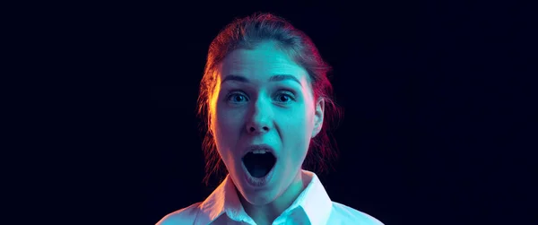 Menina chocada em camisa branca olhando para a câmera com a boca aberta isolada no fundo escuro em luz de néon azul, filtro. Conceito de emoções, moda, juventude — Fotografia de Stock