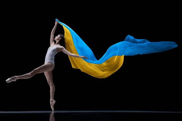 Jeune ballerine classique gracieuse dansant avec un tissu peint dans les couleurs bleu et jaune du drapeau de l'Ukraine sur fond sombre studio. Art, paix, liberté et droits — Photo