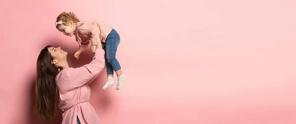 Грай. Портрет молодої жінки і маленької дівчинки, матері і дочки ізольовані на рожевому фоні студії. День матері. Концепція сім'ї, дитинства, материнства — стокове фото