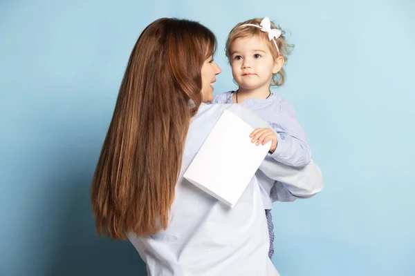 Studio photo de belle femme heureuse et petit enfant, mère et fille isolées sur fond bleu. Fête des Mères. Concept de famille, enfance — Photo