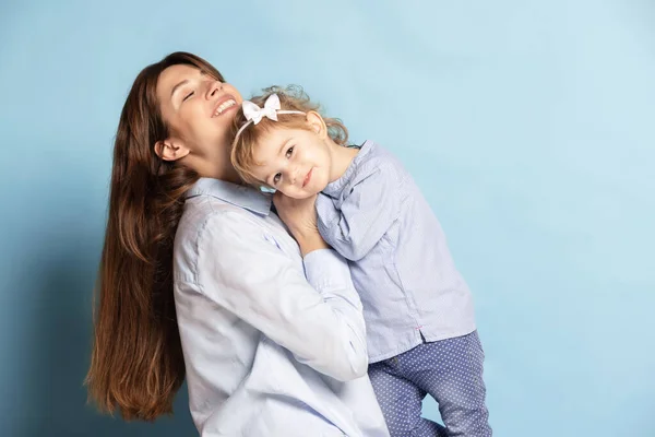 Studio photo de belle femme heureuse et petit enfant, mère et fille isolées sur fond bleu. Fête des Mères. Concept de famille, enfance — Photo